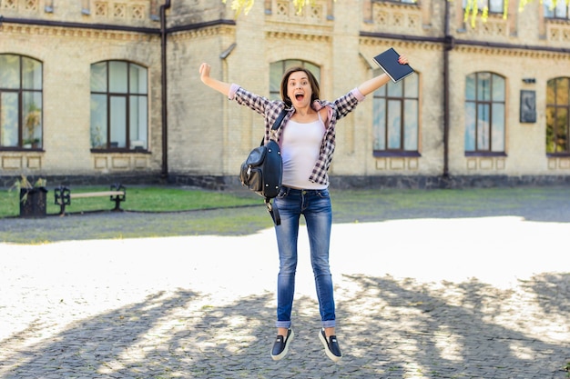 Ragazza di salto con sfondo campus libro e borsa