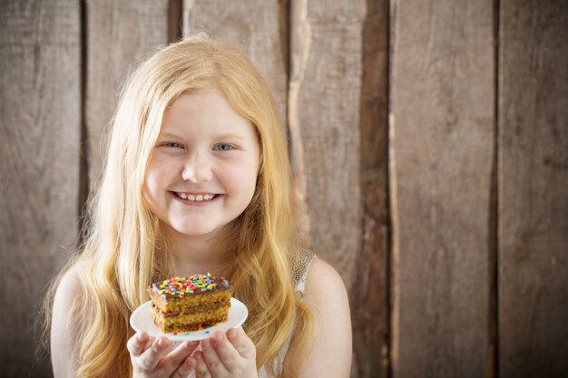 Ragazza di sorriso con la torta sulla parete di legno