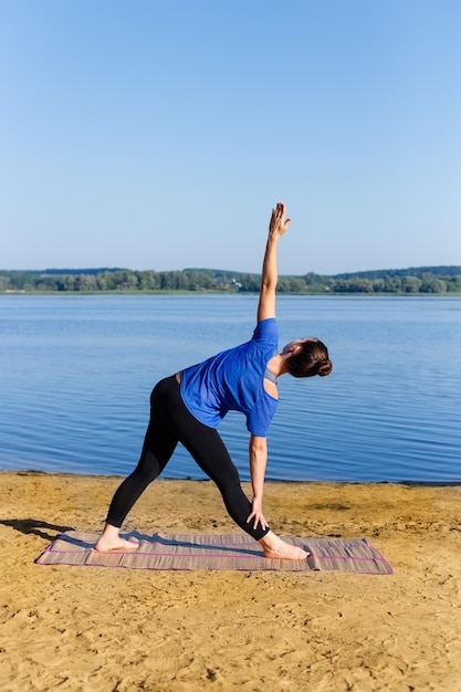 Ragazza di yoga in postura triangolare sulla riva del fiume