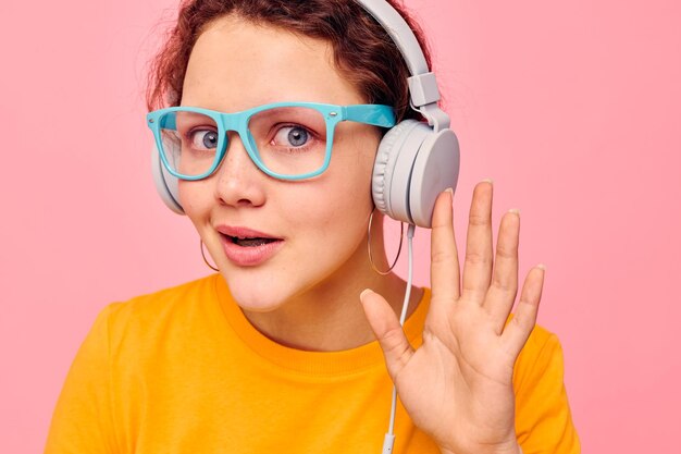 Ragazza divertente che indossa occhiali blu ascoltando musica su sfondo rosa cuffie inalterato