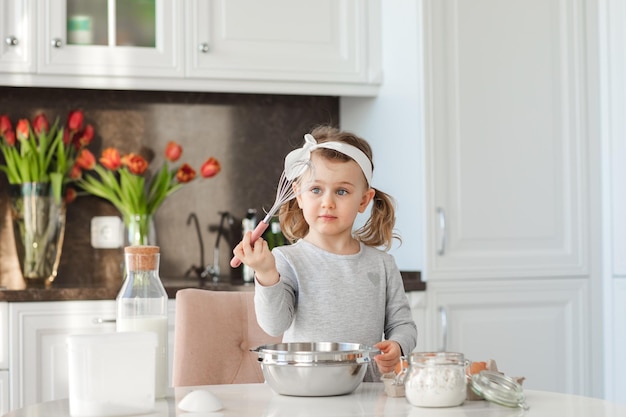 Ragazza divertente del bambino che fa la torta di Pasqua nella cucina di casa soleggiata che prepara l'impasto per la cottura