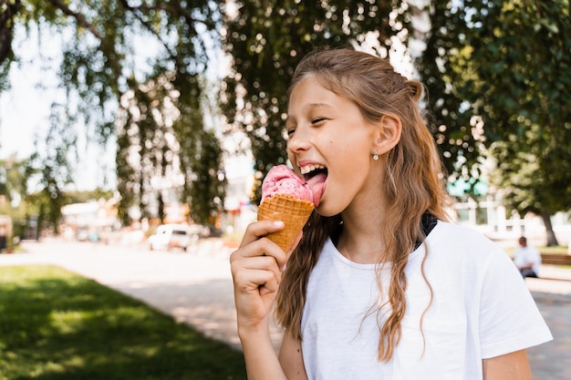 Ragazza divertente del bambino che mangia il cono gelato nella tazza della cialda Pubblicità creativa per il chiosco e il negozio del gelato