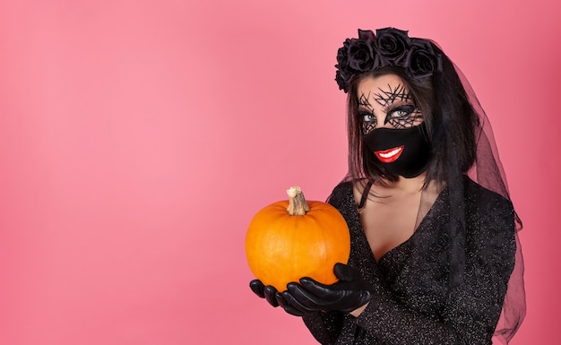 Ragazza divertente in un costume di Halloween con un sorriso stampato su una maschera nera e una zucca nelle sue mani