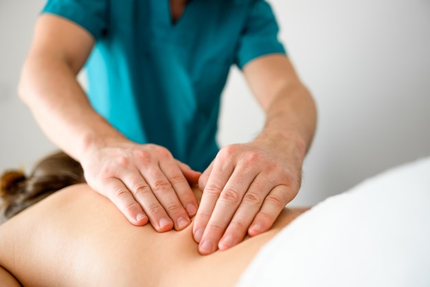 Ragazza durante il massaggio alla schiena sdraiato nella clinica del salone spa Mani del massaggiatore che eseguono la procedura di terapia del corpo per il benessere e il relax della giovane donna