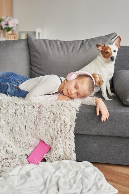 Ragazza e cane posa sul divano in cuffia, ascoltando musica con il suo smarthphone