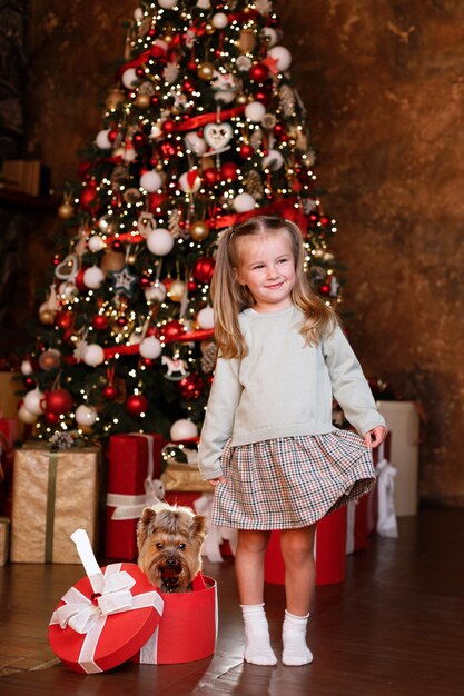 Ragazza e cucciolo con un regalo di Natale vicino all'albero di Natale