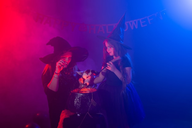 Ragazza e donna divertenti del bambino in costumi delle streghe per Halloween con il cane.