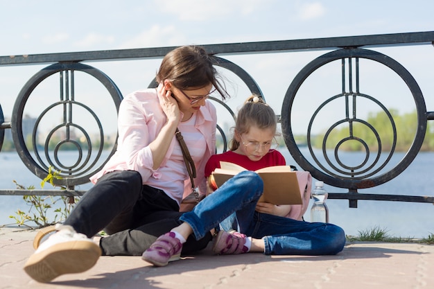 Ragazza e madre che leggono il libro. Urbano, fiume, cielo