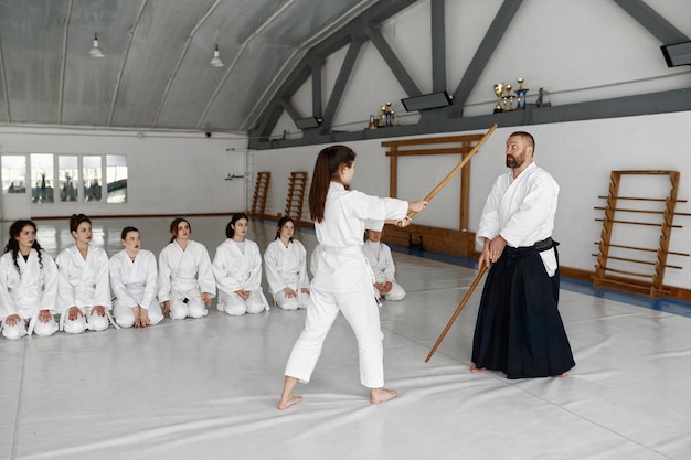 Ragazza e maestro di aikido che combattono con la spada di legno durante la lezione di arti marziali