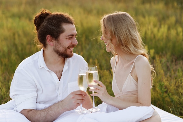 Ragazza e ragazzo biondi bevono champagne dai bicchieri e sorridono nel parco la sera al tramonto