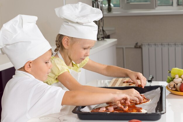 Ragazza e ragazzo che caricano gli ingredienti sulla pizza