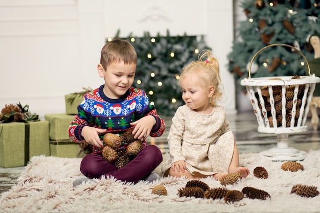 Ragazza e ragazzo che giocano sul pavimento con i coni per decorare l'albero di Natale.