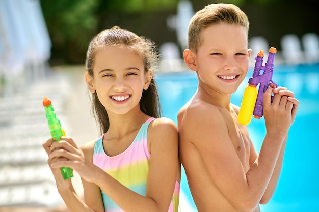 Ragazza e ragazzo con pistole ad acqua che guarda l'obbiettivo