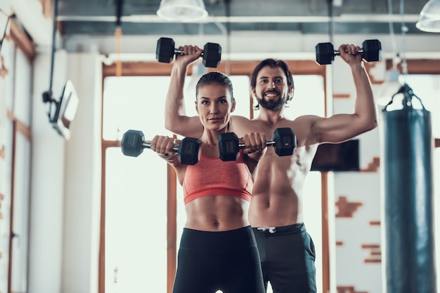 Ragazza e ragazzo in palestra facendo esercizi manubri.