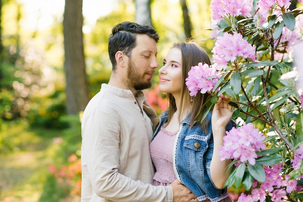 Ragazza e ragazzo, innamorati l'uno dell'altro, felici di stare insieme. Sorridono e camminano nei giardini fioriti del rododendro