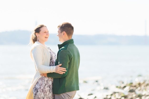 Ragazza e ragazzo si abbracciano e si guardano sulla riva del fiume in una giornata di sole