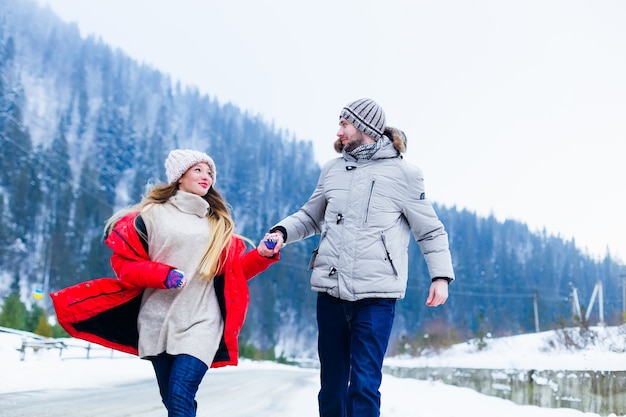 Ragazza e ragazzo si tengono per mano e corrono lungo la strada nelle montagne invernali