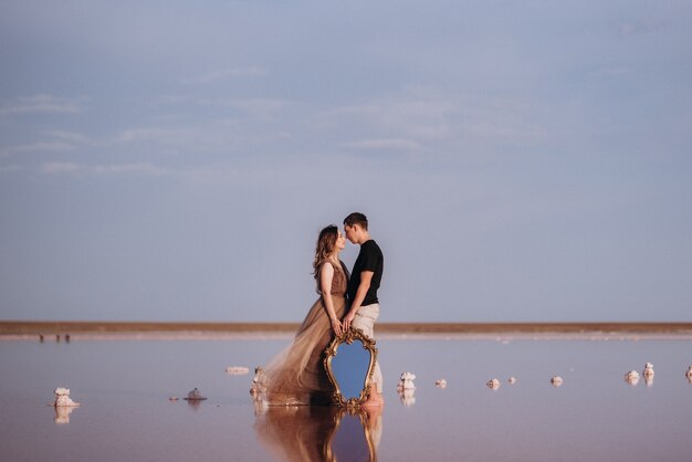 Ragazza e un ragazzo sulla riva di un lago salato rosa al tramonto