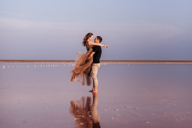 Ragazza e un ragazzo sulla riva di un lago salato rosa al tramonto