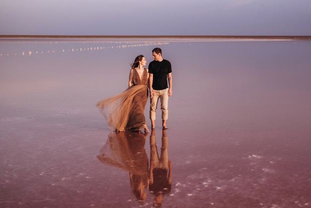 Ragazza e un ragazzo sulla riva di un lago salato rosa al tramonto