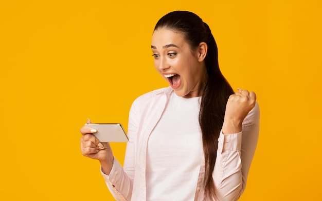 Ragazza Eccitata Che Gesticola Sì E Guarda Lo Smartphone Girato In Studio