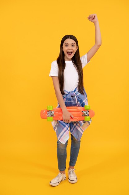 Ragazza eccitata con pennyboard felice urlando facendo gesto vincente sfondo giallo skateboard