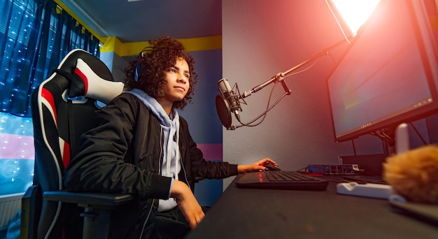 Ragazza eccitata del giocatore in cuffia con un microfono che gioca a un videogioco online sul personal computer Parlando con altri giocatori La stanza e il PC hanno luci colorate calde al neon a led Serata accogliente a casa