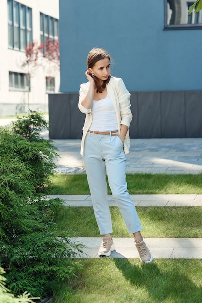 Ragazza elegante in abito casual leggero in piedi vicino alla parete grigia dell'edificio moderno