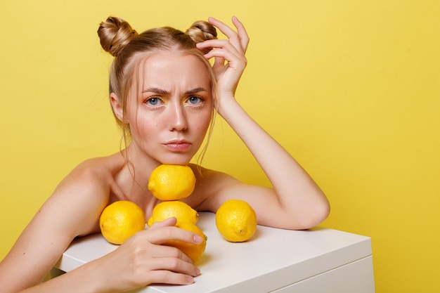 Ragazza emotiva con limoni su una parete gialla