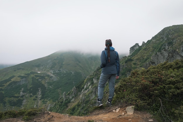 Ragazza escursionista con uno zaino si erge su una roccia in montagna Trekking Vita Escursione attraverso i Carpazi Verdi pendii di montagna e rododendro in fiore