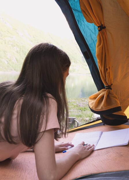 Ragazza escursionista in tenda e scrive in un diario montagne sullo sfondo