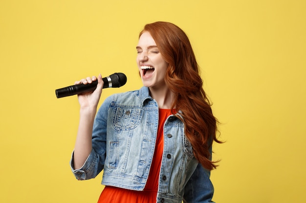 Ragazza espressiva che canta con un microfono, fondo giallo luminoso isolato.