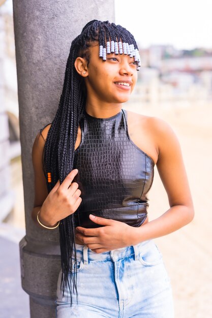 Ragazza etnica nera con trecce con top in pelle e pantaloni da cowboy. Godersi le vacanze estive vicino alla spiaggia, PosÃ© con un look seducente