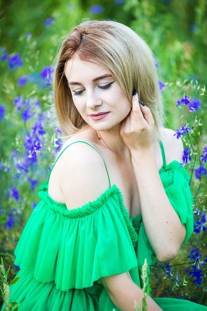 Ragazza europea bionda in un vestito verde sulla natura con fiori blu