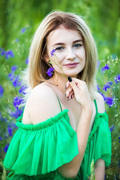 Ragazza europea bionda in un vestito verde sulla natura con fiori blu