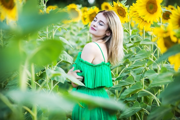 Ragazza europea bionda in un vestito verde sulla natura con i girasoli