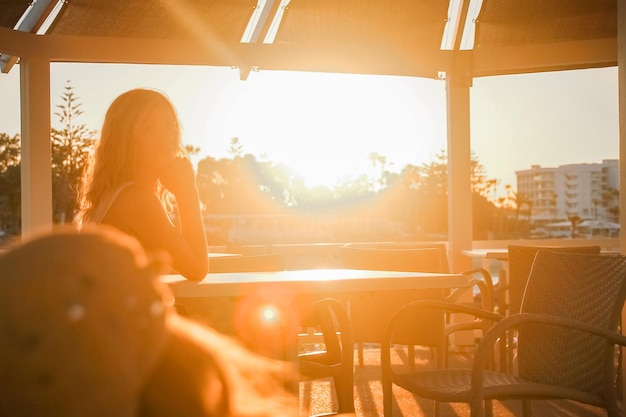 Ragazza felice a un tavolo in riva al mare al tramonto