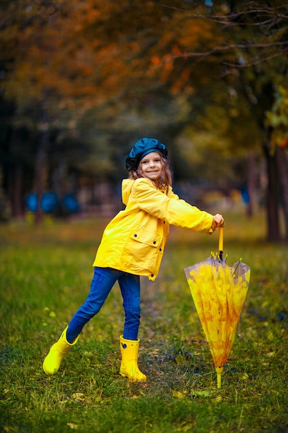 Ragazza felice bambino divertente con ombrello multicolore in stivali di gomma al parco d'autunno.