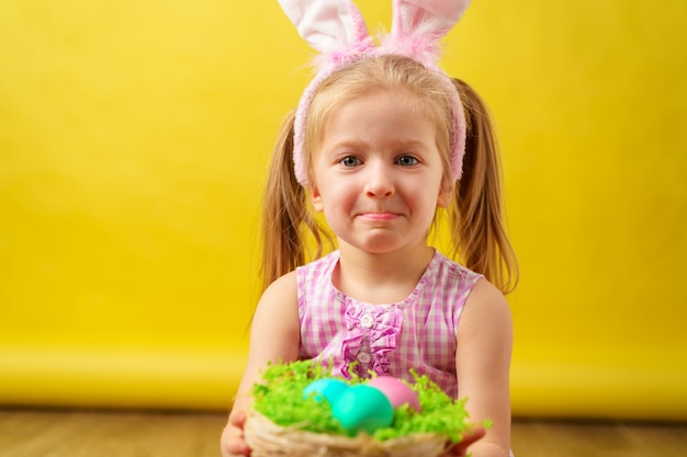 Ragazza felice bionda con le orecchie del coniglietto e canestro delle uova per Pasqua