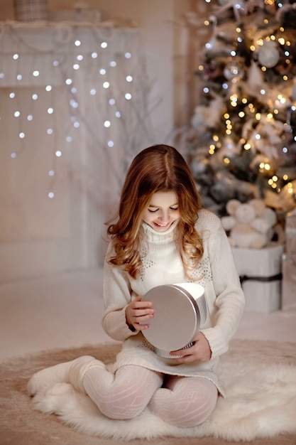 Ragazza felice che apre i regali di Natale davanti al caminetto in un accogliente soggiorno buio la vigilia di Natale