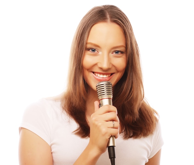 Ragazza felice che canta. Donna di bellezza che indossa t-shirt bianca con microfono su sfondo bianco.