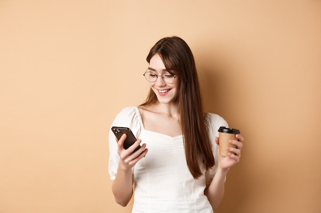 Ragazza felice che chiacchiera al telefono e beve caffè indossando occhiali e camicetta bianca che sorride allo smartph...