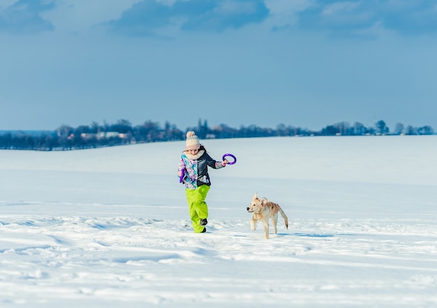 Ragazza felice che funziona con il simpatico cane nella neve scintillante