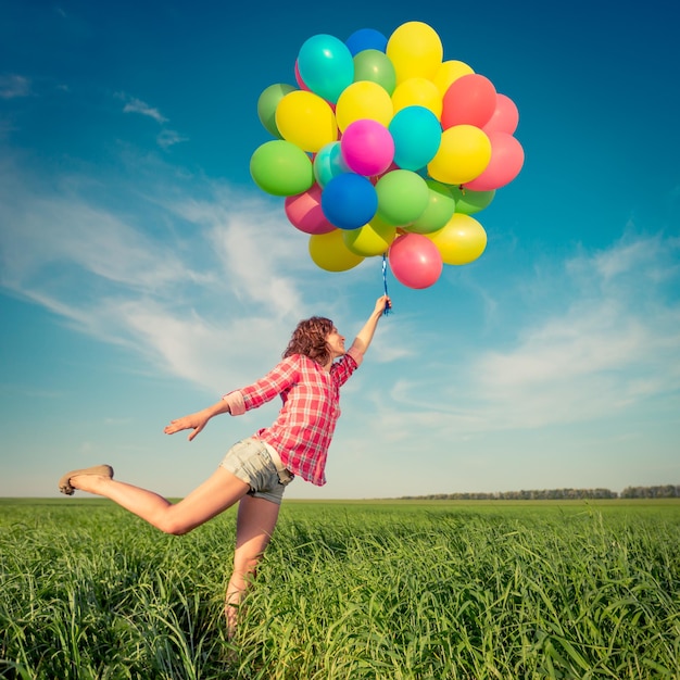 Ragazza felice che gioca con palloncini colorati giocattolo all'aperto Giovane donna divertirsi nel campo di primavera verde su sfondo blu cielo Concetto di libertà