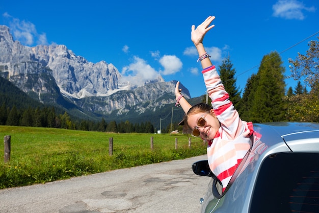 Ragazza felice che guarda fuori dal finestrino dell'auto e le montagne sullo sfondo. Dolomiti, Italia