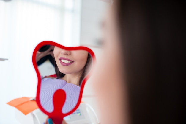 Ragazza felice che osserva nello specchio un sorriso in odontoiatria.