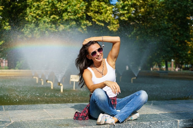 Ragazza felice che posa contro la fontana dello sfondo in una giornata di sole in abiti casual