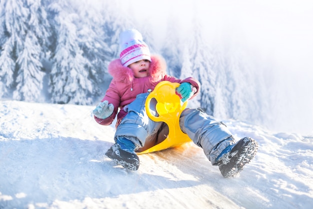 Ragazza felice che sledding all'aperto il chiaro giorno di inverno