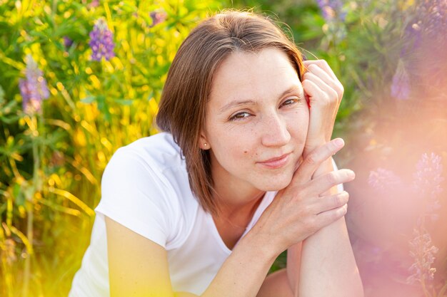 Ragazza felice che sorride all'aperto. Bella giovane donna brunete che riposa sul campo estivo con sfondo verde di fiori selvatici in fiore.