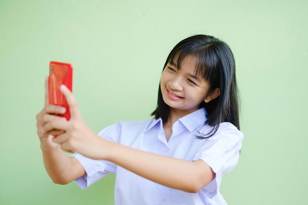 Ragazza felice che utilizza smartphone su sfondo verde, ragazza asiatica, scolara.